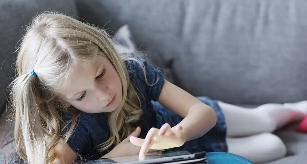 flicka ligger på soffan med en surfplatta i handen